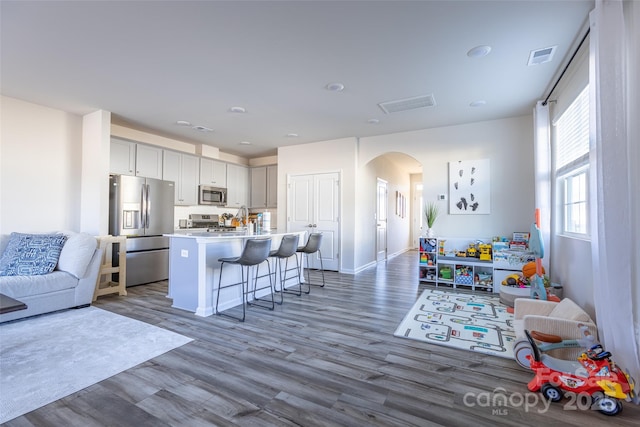 kitchen with a center island with sink, arched walkways, appliances with stainless steel finishes, a breakfast bar area, and light countertops