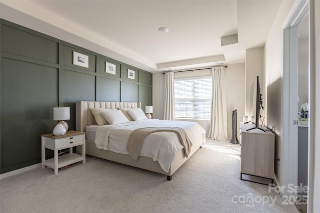 bedroom featuring a tray ceiling, a decorative wall, and light colored carpet