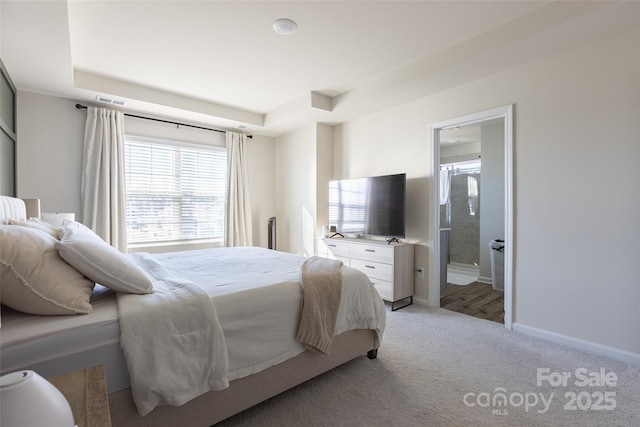 bedroom featuring light carpet, visible vents, baseboards, a raised ceiling, and ensuite bath