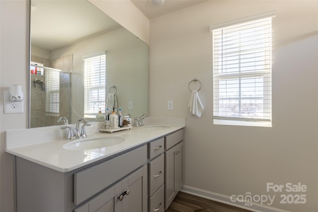 bathroom with double vanity, a shower stall, baseboards, and a sink