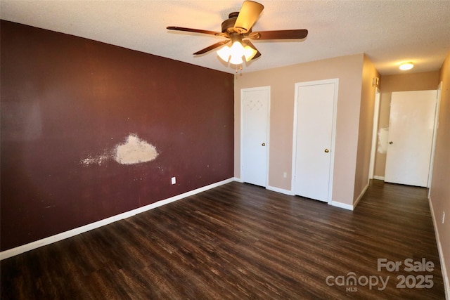 unfurnished bedroom with a textured ceiling, ceiling fan, dark wood finished floors, and baseboards