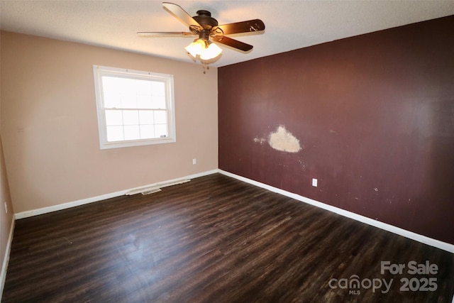 spare room with visible vents, dark wood-style flooring, a ceiling fan, and baseboards