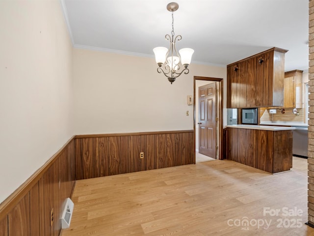 kitchen featuring a chandelier, light wood-style flooring, a peninsula, wainscoting, and brown cabinetry