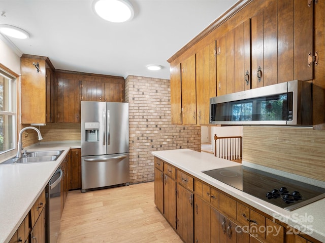 kitchen with light wood-style flooring, appliances with stainless steel finishes, a sink, light countertops, and backsplash