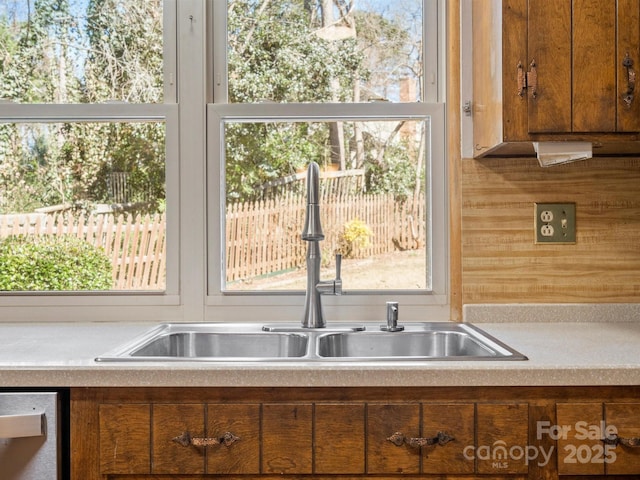 kitchen featuring stainless steel dishwasher, brown cabinetry, a sink, and light countertops