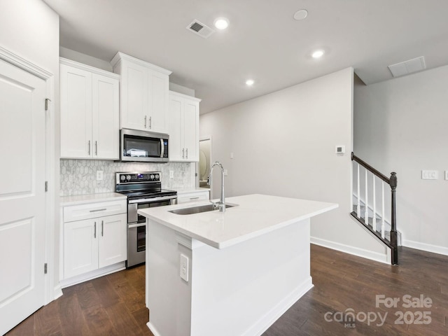 kitchen with a sink, appliances with stainless steel finishes, backsplash, dark wood-style floors, and an island with sink