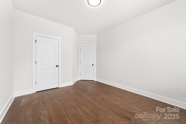 unfurnished room featuring baseboards and dark wood-type flooring