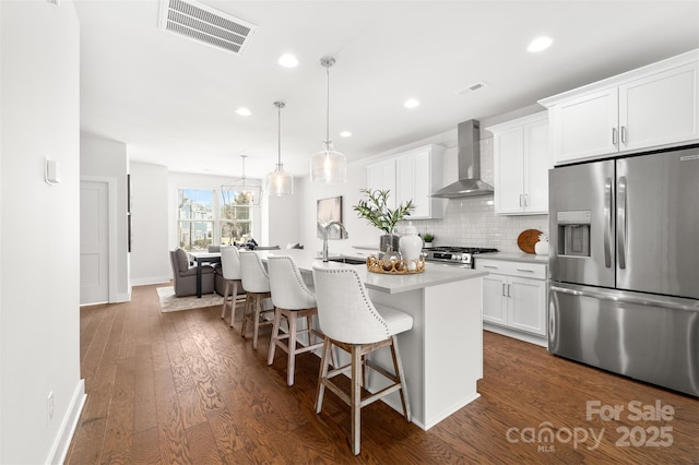 kitchen featuring a kitchen bar, visible vents, appliances with stainless steel finishes, a kitchen island with sink, and wall chimney exhaust hood