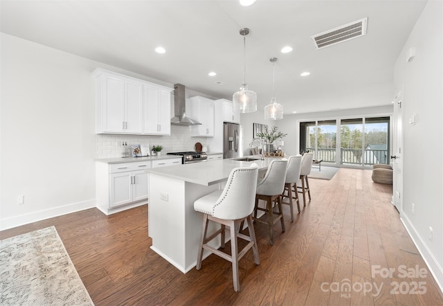 kitchen with stainless steel appliances, a sink, visible vents, wall chimney exhaust hood, and an island with sink