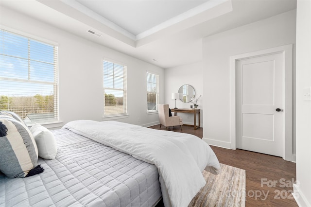 bedroom with a raised ceiling, visible vents, baseboards, and wood finished floors