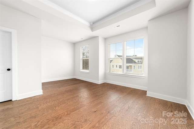 spare room featuring a raised ceiling, visible vents, baseboards, and wood finished floors