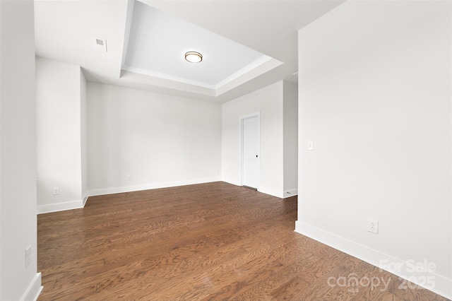 empty room with a tray ceiling, visible vents, baseboards, and wood finished floors