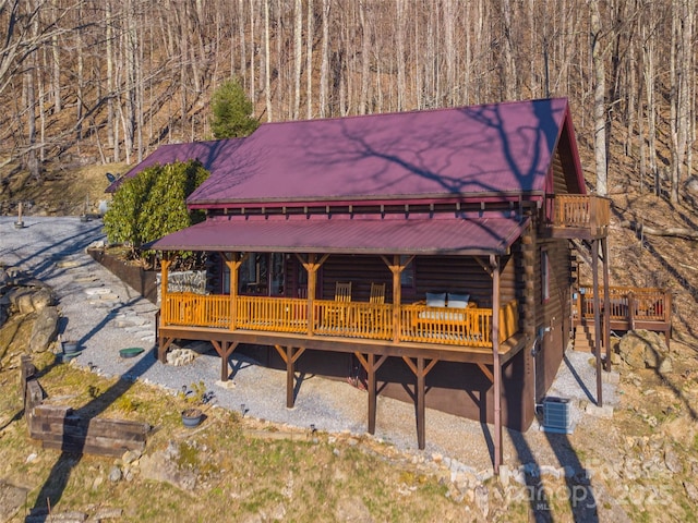 view of front facade featuring metal roof, central AC unit, log siding, and a wooden deck