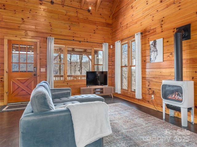 living room with high vaulted ceiling, a wood stove, wooden ceiling, and wooden walls