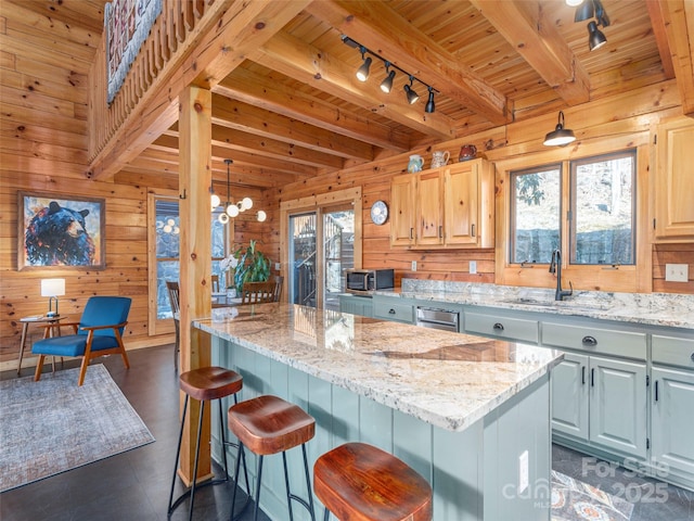 kitchen featuring a kitchen island, wood walls, a sink, and light stone countertops