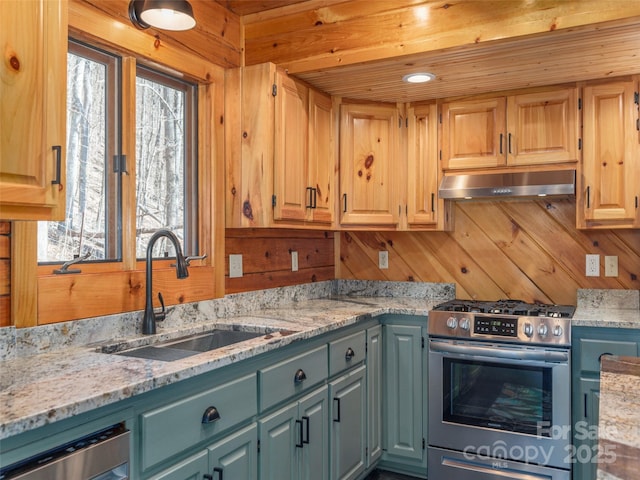 kitchen featuring wooden walls, under cabinet range hood, stainless steel appliances, a sink, and light stone countertops