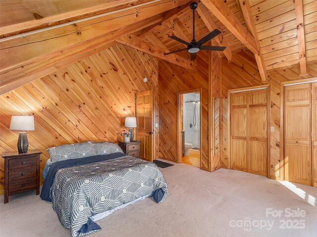 bedroom with beam ceiling, light carpet, wooden walls, ensuite bath, and wooden ceiling