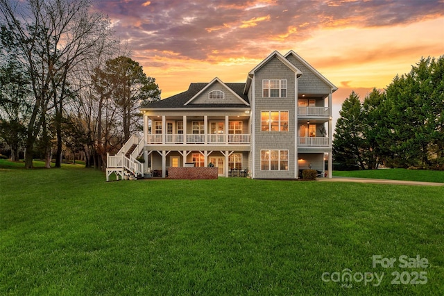 back of house at dusk featuring driveway, stairs, and a yard