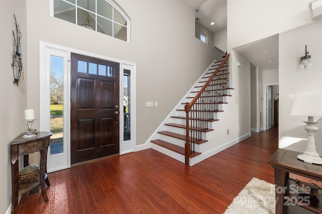 foyer with a healthy amount of sunlight, baseboards, a high ceiling, and wood finished floors