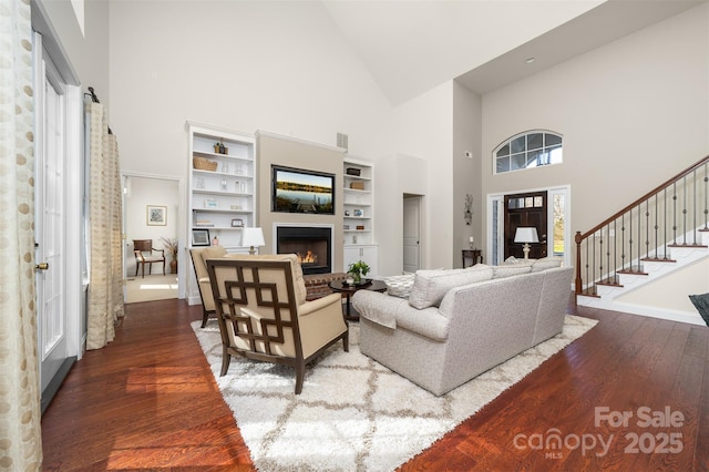 living room with visible vents, a glass covered fireplace, lofted ceiling, stairway, and hardwood / wood-style floors