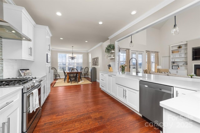 kitchen with stainless steel appliances, a sink, open floor plan, light countertops, and wall chimney range hood