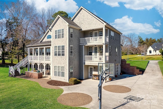 rear view of property with stairway, concrete driveway, a lawn, and a balcony