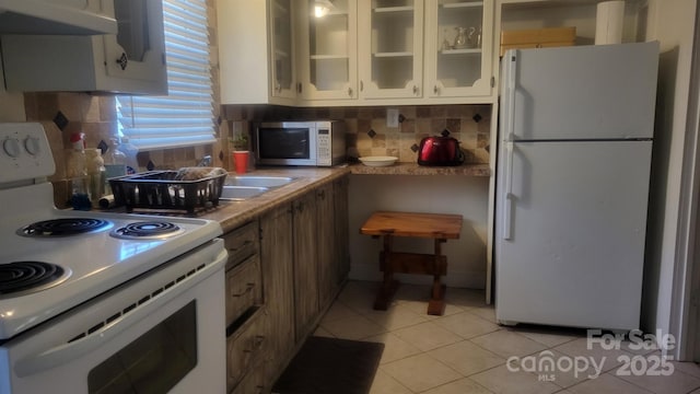 kitchen featuring white appliances, light tile patterned floors, light countertops, under cabinet range hood, and backsplash