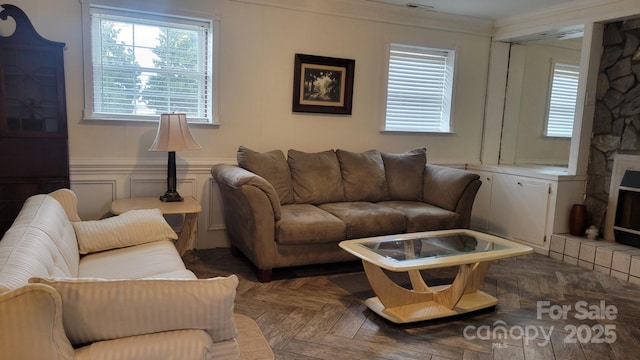 living room with a healthy amount of sunlight, ornamental molding, and a fireplace with raised hearth