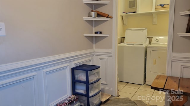 washroom with a wainscoted wall, light tile patterned floors, visible vents, separate washer and dryer, and laundry area