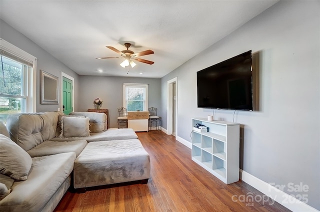 living room with ceiling fan, baseboards, and wood finished floors