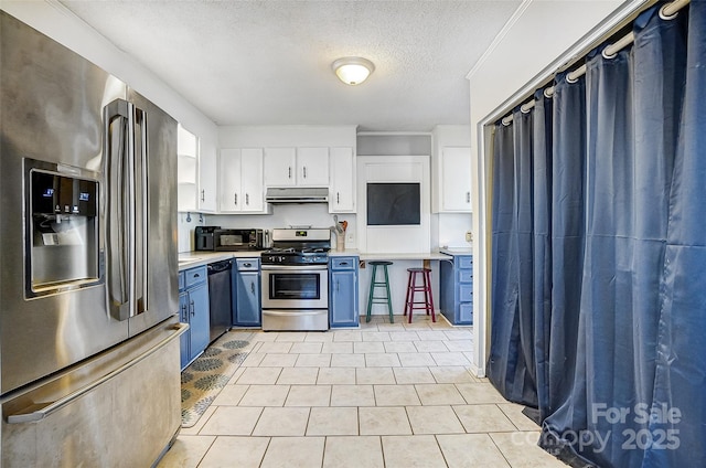 kitchen featuring white cabinets, blue cabinets, stainless steel appliances, light countertops, and under cabinet range hood