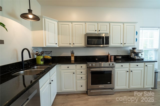 kitchen featuring dark stone countertops, white cabinetry, light wood-style floors, stainless steel appliances, and a sink