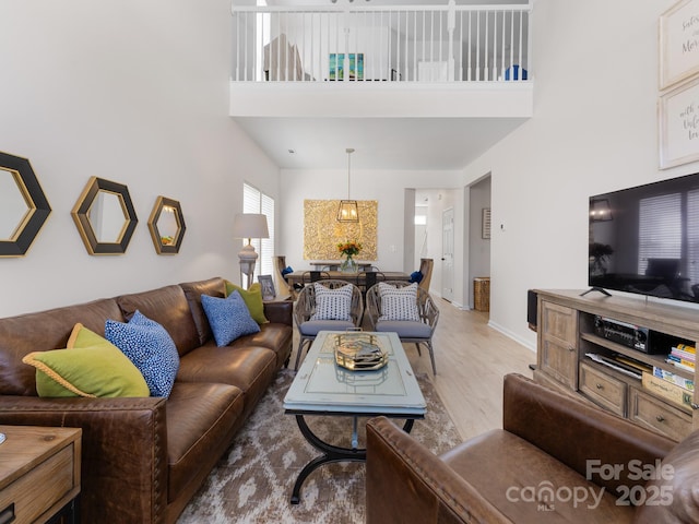 living room with a high ceiling, light wood finished floors, and baseboards