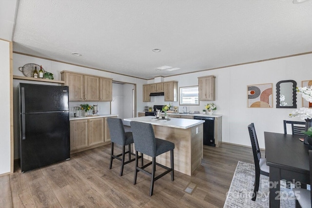 kitchen featuring dark wood-type flooring, a kitchen island, light countertops, black appliances, and a kitchen bar