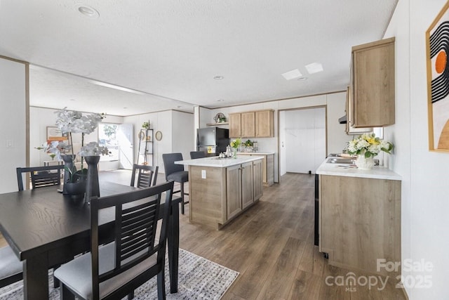 kitchen with dark wood-style flooring, light countertops, freestanding refrigerator, a kitchen island, and a textured ceiling