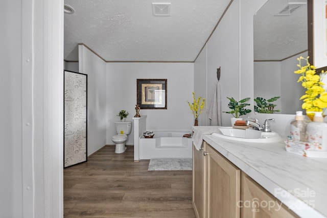 bathroom with a textured ceiling, toilet, wood finished floors, vanity, and a bath