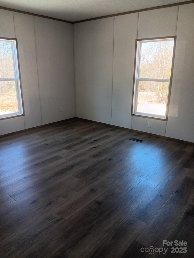 spare room with a wealth of natural light, visible vents, and dark wood finished floors