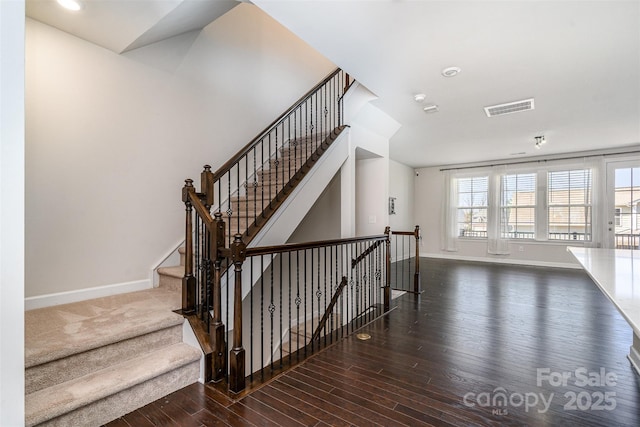 staircase with baseboards, visible vents, and wood finished floors