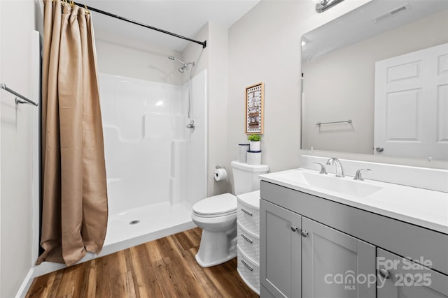 bathroom with visible vents, toilet, wood finished floors, vanity, and a shower stall