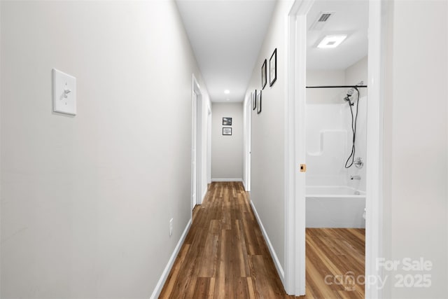 corridor with baseboards, visible vents, and wood finished floors