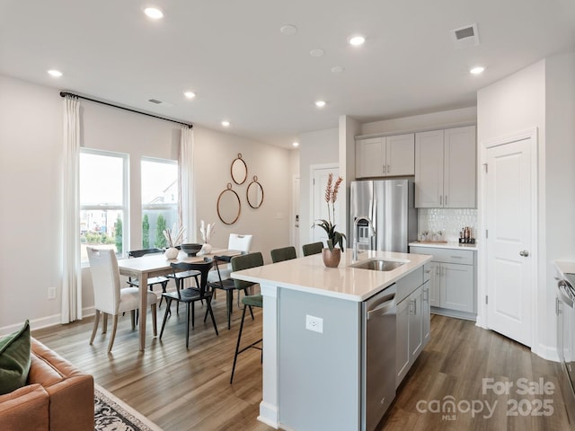 kitchen featuring a center island with sink, light countertops, visible vents, appliances with stainless steel finishes, and a kitchen bar