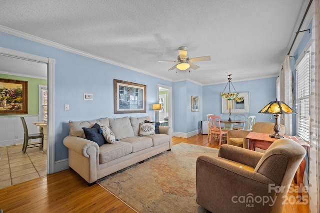 living area with ornamental molding, light wood-style flooring, a textured ceiling, and a ceiling fan