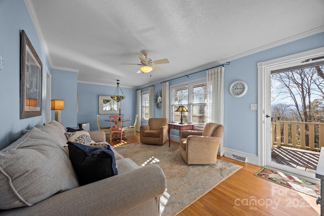 living area featuring light wood finished floors, visible vents, ceiling fan, ornamental molding, and a textured ceiling