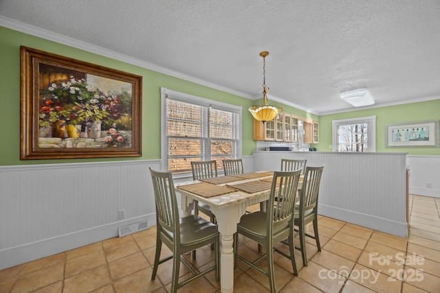 dining room featuring crown molding, visible vents, a textured ceiling, and wainscoting