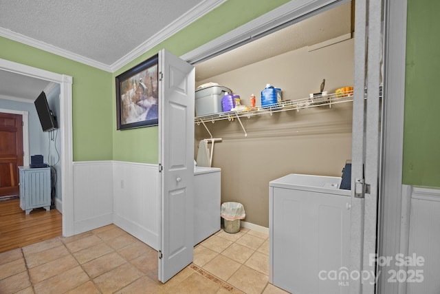 laundry area featuring a textured ceiling, a wainscoted wall, laundry area, washer / dryer, and crown molding