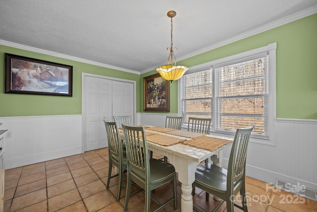 dining room with visible vents, ornamental molding, a textured ceiling, and wainscoting