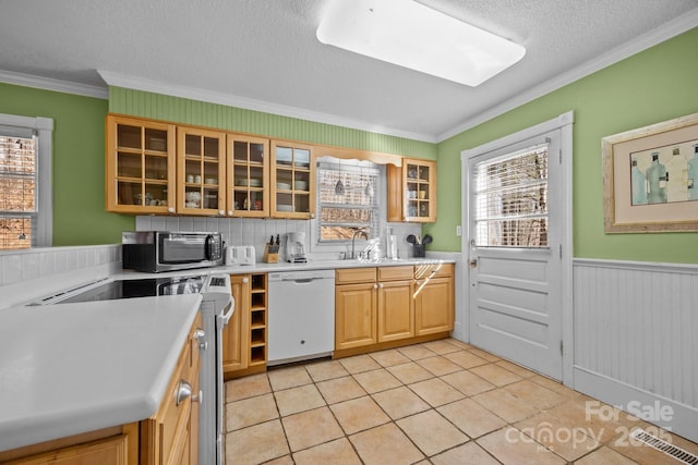 kitchen with light countertops, stainless steel microwave, glass insert cabinets, wainscoting, and white dishwasher