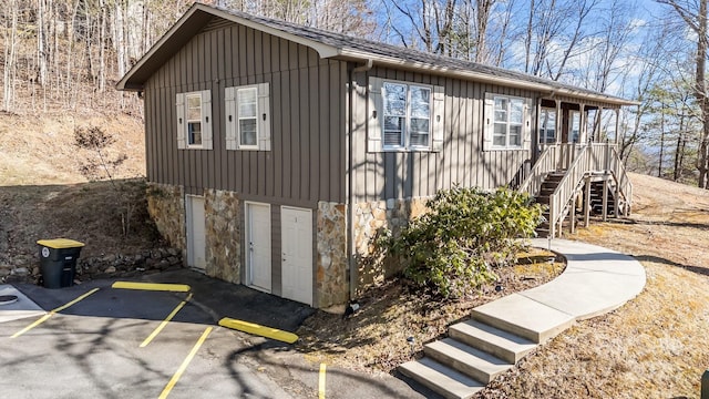 view of property exterior featuring a garage, stone siding, stairway, and board and batten siding