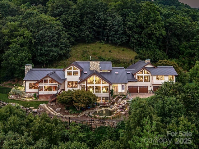 rear view of property with a view of trees, stone siding, a chimney, metal roof, and a standing seam roof