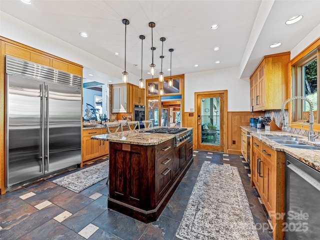 kitchen with decorative light fixtures, stainless steel appliances, a kitchen island, a sink, and light stone countertops